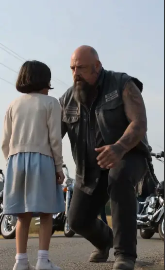 The road looked empty, but the little girl kept staring behind her like something terrible was still coming. She stood in the cold gray light in a simple blue dress, cheeks soaked with tears, hands shaking so badly she could barely point.